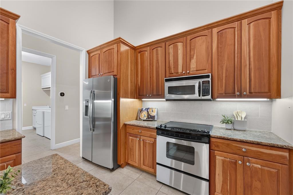 A kitchen features wood cabinets, stainless steel appliances, granite countertops, and a tile backsplash — 2816 N PRESTWICK WAY, LECANTO, FL