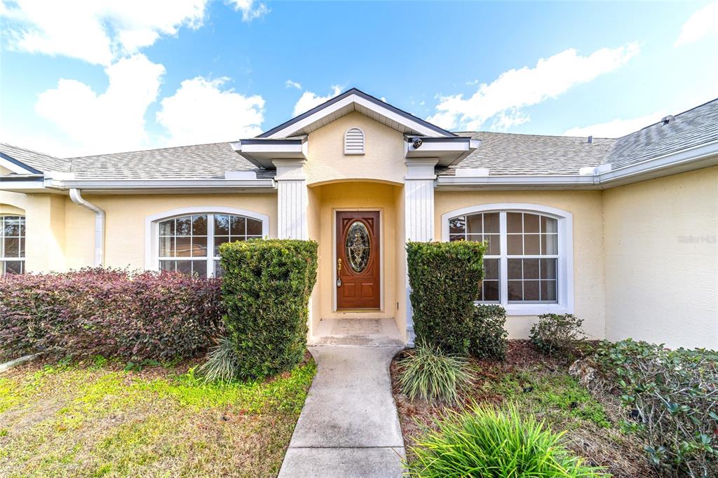 The exterior of a single-story house features a tan stucco facade and a front walkway — 9611 SW 45TH AVENUE, OCALA, FL