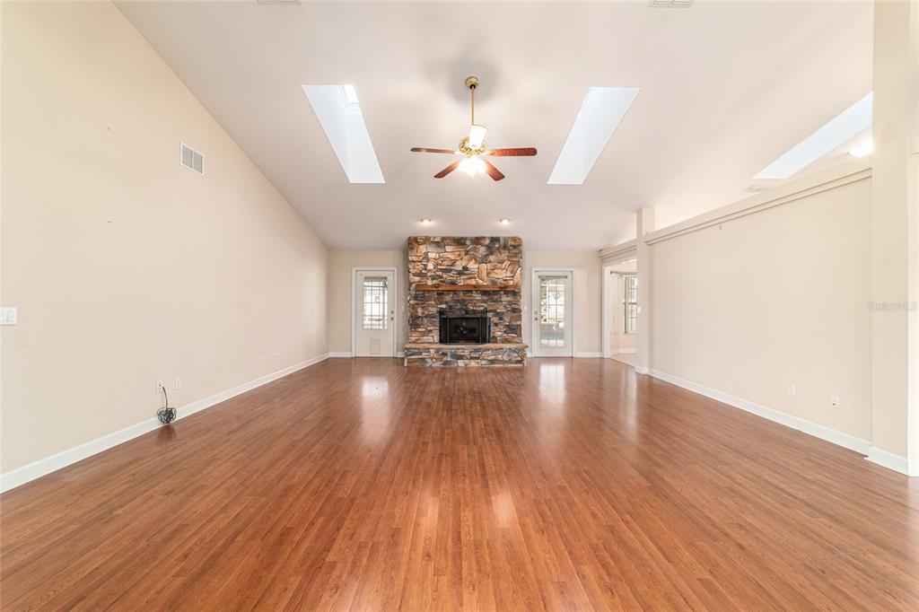 A spacious living room features vaulted ceilings, skylights, a stone fireplace, and wood flooring — 9611 SW 45TH AVENUE, OCALA, FL