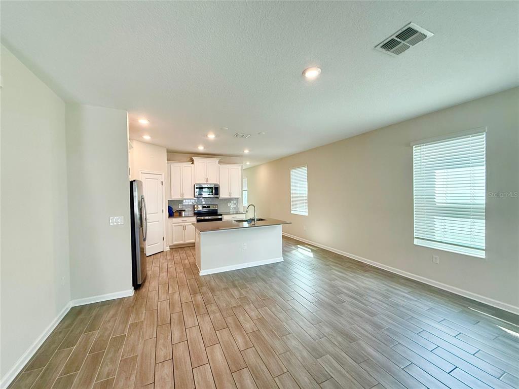 An open-concept kitchen and living area features white cabinetry, a center island, and wood-look flooring — 1374 VISCAYA COVE BOULEVARD, WINTER GARDEN, FL