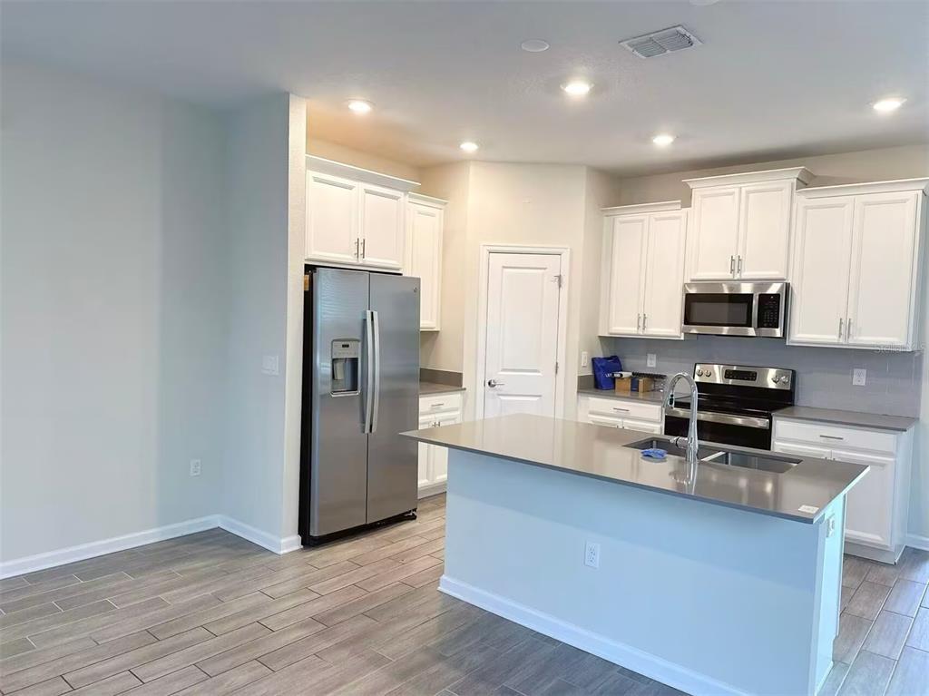 A modern kitchen features white cabinets, stainless steel appliances, a gray island, and tile flooring — 1374 VISCAYA COVE BOULEVARD, WINTER GARDEN, FL