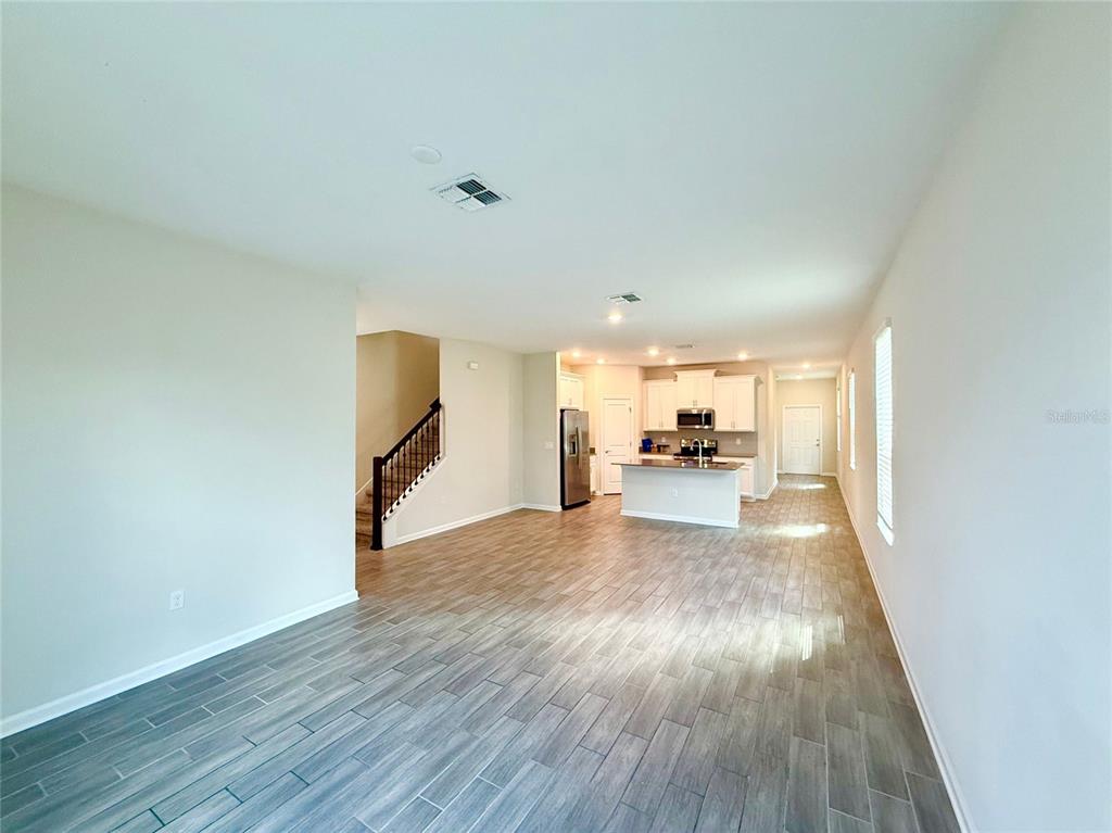 An open-concept living area features wood-look tile flooring, a staircase, and a kitchen with an island — 1374 VISCAYA COVE BOULEVARD, WINTER GARDEN, FL