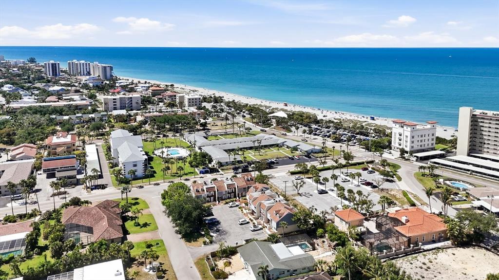 An aerial view shows a coastal neighborhood with multi-story buildings, parking lots, and a beach — 744 CADIZ ROAD UNIT 8, VENICE, FL