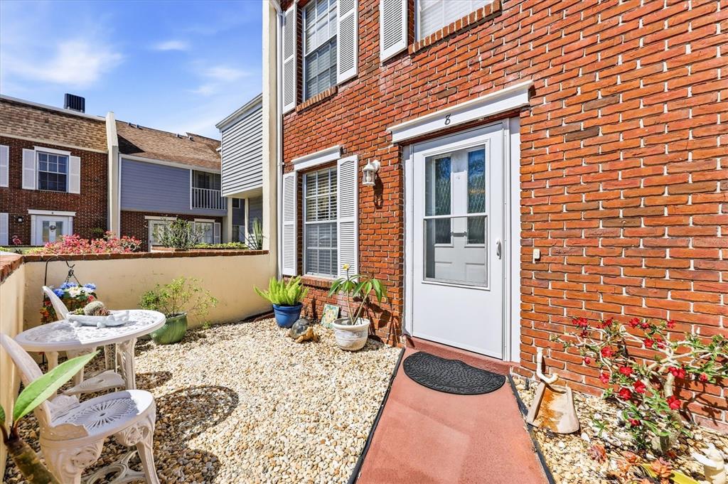 A brick townhouse exterior features a small gravel patio with white furniture and potted plants — 744 CADIZ ROAD UNIT 8, VENICE, FL