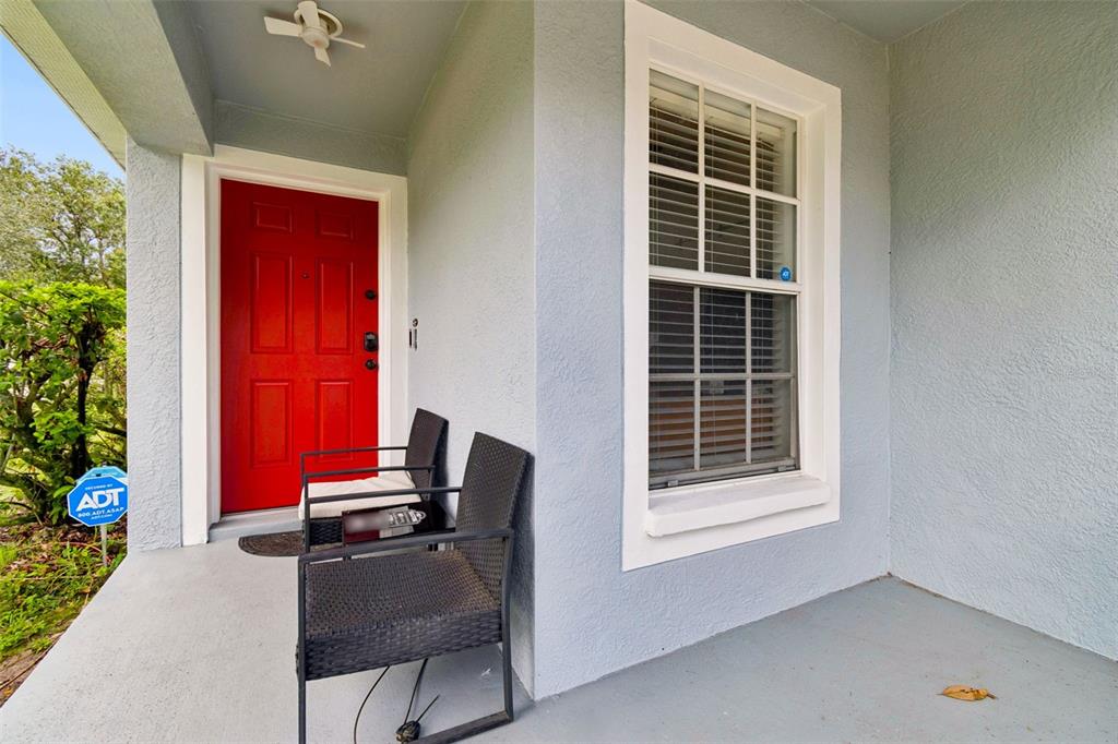A covered front porch features a bright red door, two black chairs, and a window — 10731 NAVIGATION DRIVE, RIVERVIEW, FL