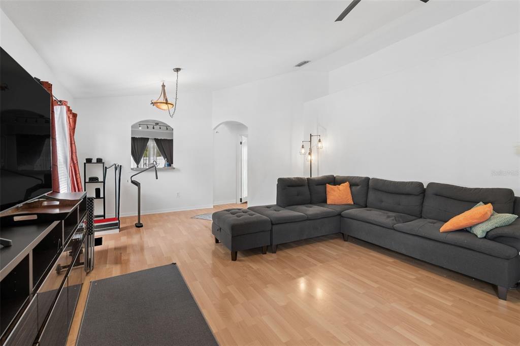 A living room features light wood flooring, a large gray sectional sofa, and white walls — 10731 NAVIGATION DRIVE, RIVERVIEW, FL