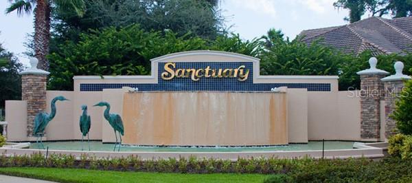 A stone and stucco entrance sign for The Sanctuary features a water fountain and bird statues — 7 SABAL BEND, PALM COAST, FL
