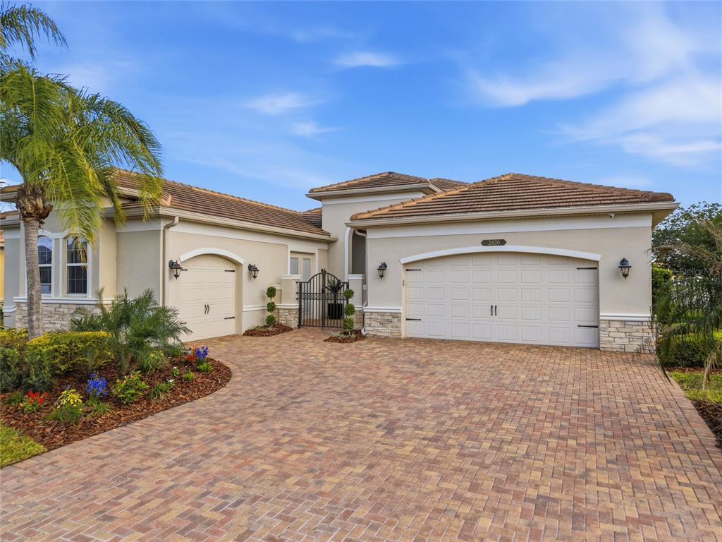 A single-story house with a paved driveway, two garage doors, and a gated courtyard entrance — 2420 COCO PALM CIRCLE, WESLEY CHAPEL, FL