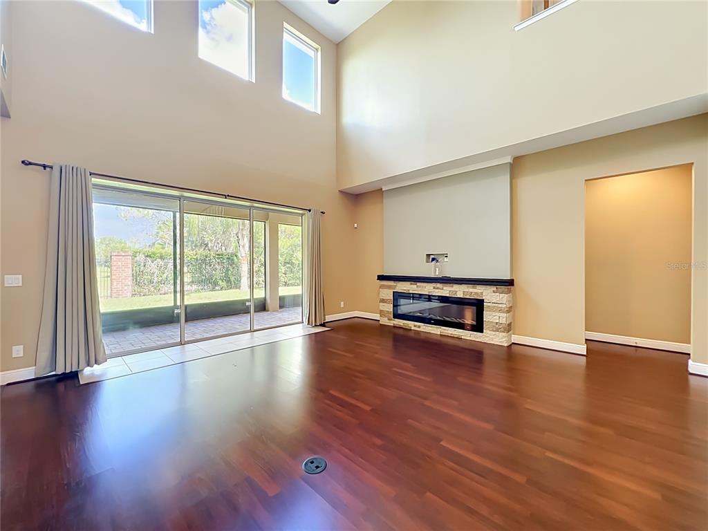 A living room features high ceilings, dark hardwood floors, a stone fireplace, and sliding glass doors — 1315 DUSTY PINE DRIVE, APOPKA, FL