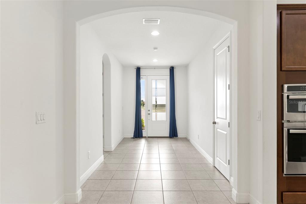 A tiled hallway leads to a front door framed by blue curtains under an archway — 3918 GAVIOTA DRIVE, RUSKIN, FL
