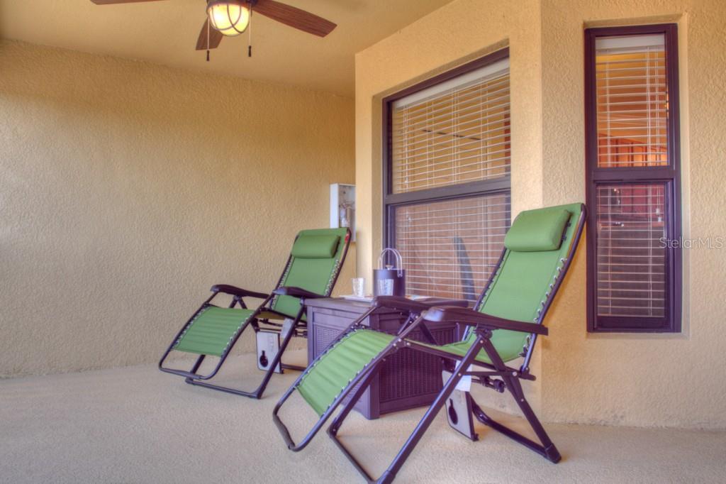 Two green lounge chairs sit on a covered patio next to a small side table — 7305 RIVER HAMMOCK DRIVE UNIT 206, BRADENTON, FL