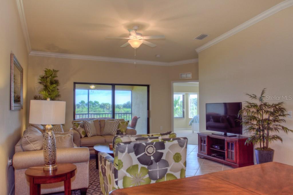 A living room features a ceiling fan, tiled floors, a television, and a sliding glass door — 7305 RIVER HAMMOCK DRIVE UNIT 206, BRADENTON, FL