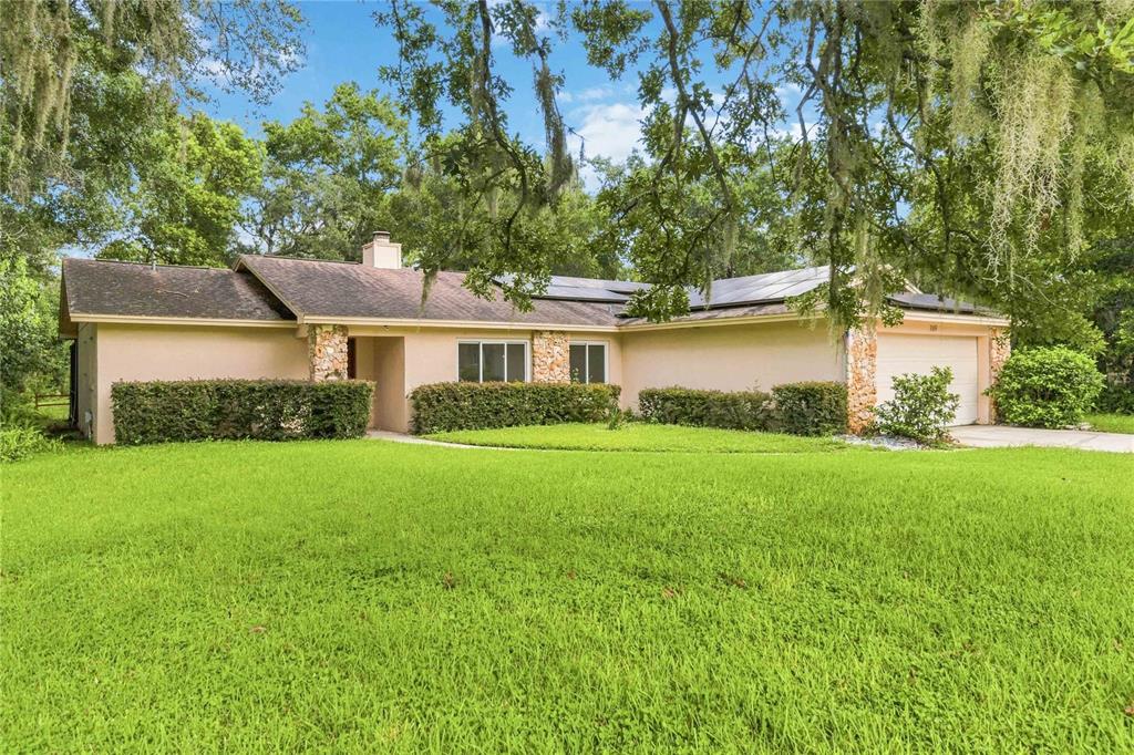 A single-story house with a tan exterior, stone accents, and solar panels on the roof — 169 DUNCAN TRAIL, LONGWOOD, FL