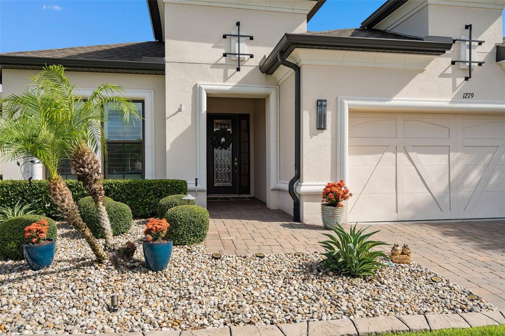 The exterior of a beige house features a paved walkway, a garage, and landscaped garden beds — 1279 ZEEK RIDGE STREET, CLERMONT, FL