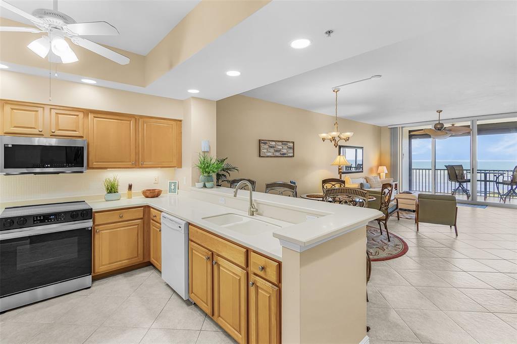 A kitchen with light wood cabinets and white countertops opens into a dining and living area — 3321 SUNSET KEY CIRCLE UNIT 508, PUNTA GORDA, FL