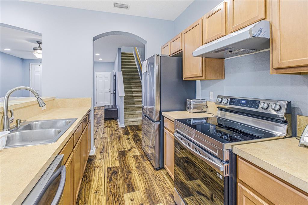 A kitchen with light wood cabinets, stainless steel appliances, and wood-look flooring leads to stairs — 3690 CRESWICK CIRCLE UNIT B, ORANGE PARK, FL