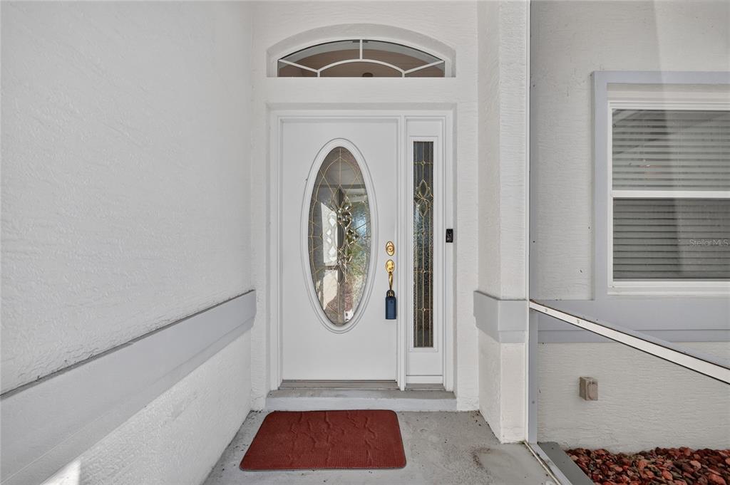 A white front door with an oval glass insert and a sidelight under a transom window — 5049 ST ANDREWS ARCADE, LEESBURG, FL