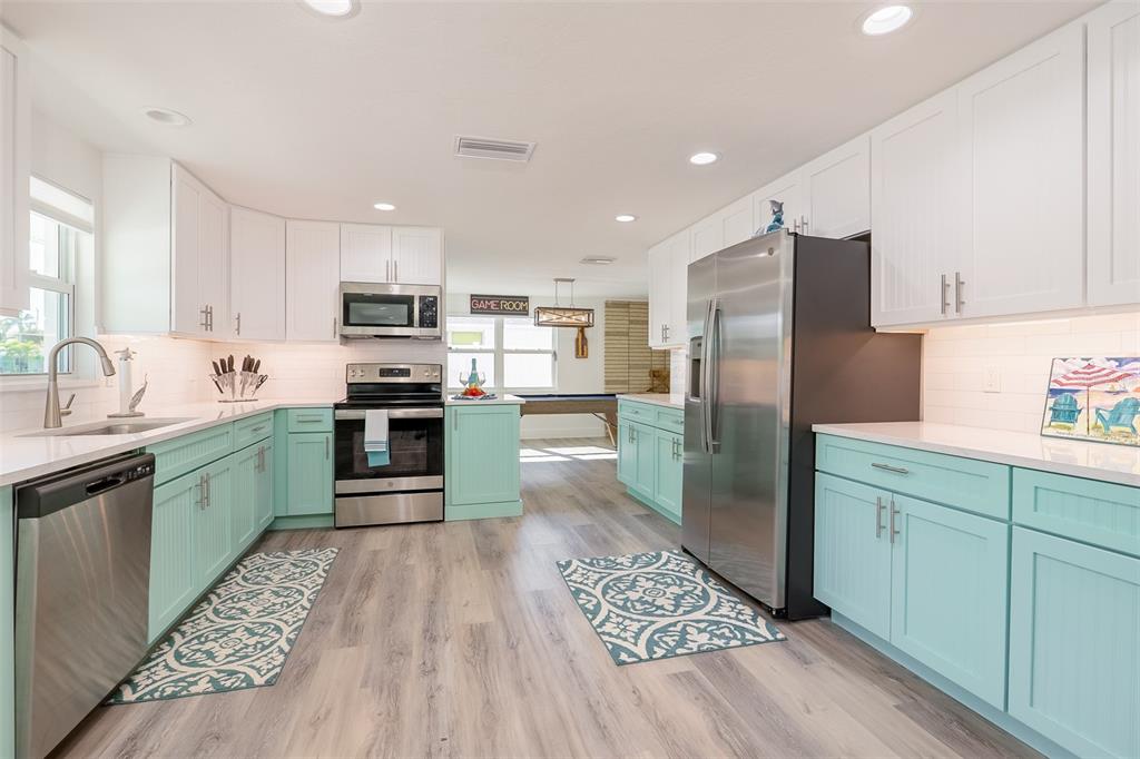 A kitchen features white upper cabinets, mint green lower cabinets, stainless steel appliances, and wood flooring — 408 71ST STREET, HOLMES BEACH, FL