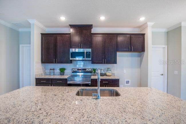 A kitchen features dark wood cabinets, granite countertops, and a stainless steel sink and stove — 39 POPLAR DRIVE, PALM COAST, FL