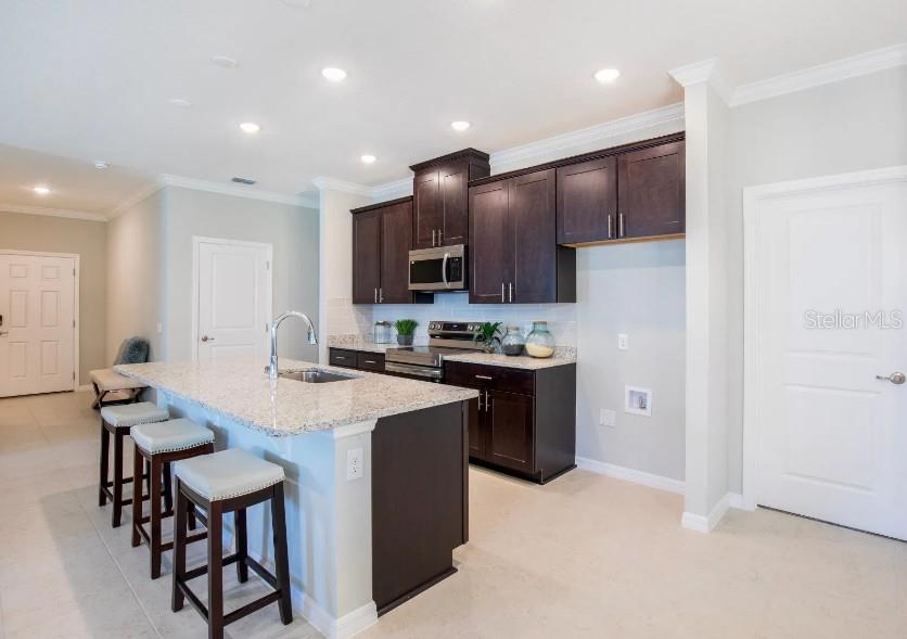 A kitchen features dark wood cabinets, granite countertops, a center island with stools, and tile flooring — 39 POPLAR DRIVE, PALM COAST, FL