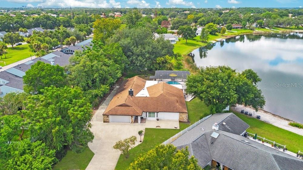 An aerial view shows a single-story house with a brown roof, pool, and lakefront yard — 8142 CHIANTI DRIVE, ORLANDO, FL