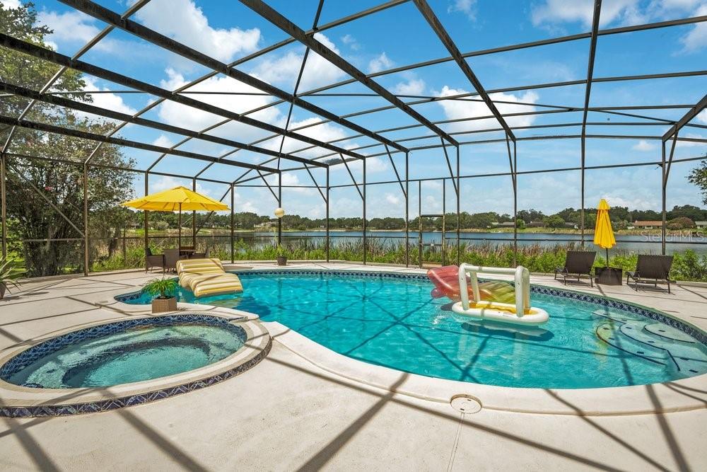 A screened-in pool and spa overlook a lake with patio furniture and yellow umbrellas — 8142 CHIANTI DRIVE, ORLANDO, FL