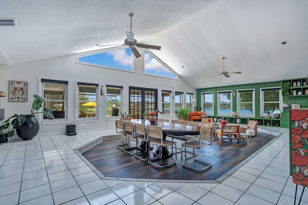 A spacious dining room features a sunken wood floor, vaulted ceilings, and large windows overlooking water — 8142 CHIANTI DRIVE, ORLANDO, FL