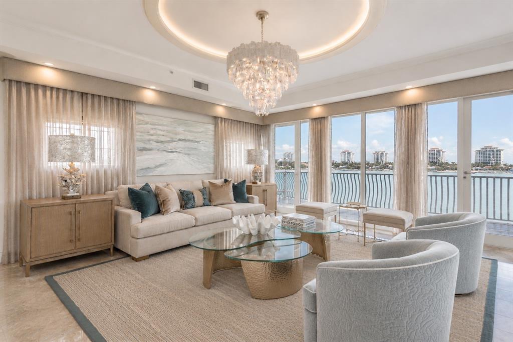 A living room features a tiered chandelier, a beige sofa, glass coffee tables, and balcony views — 200 SKIFF POINT UNIT 501, CLEARWATER BEACH, FL
