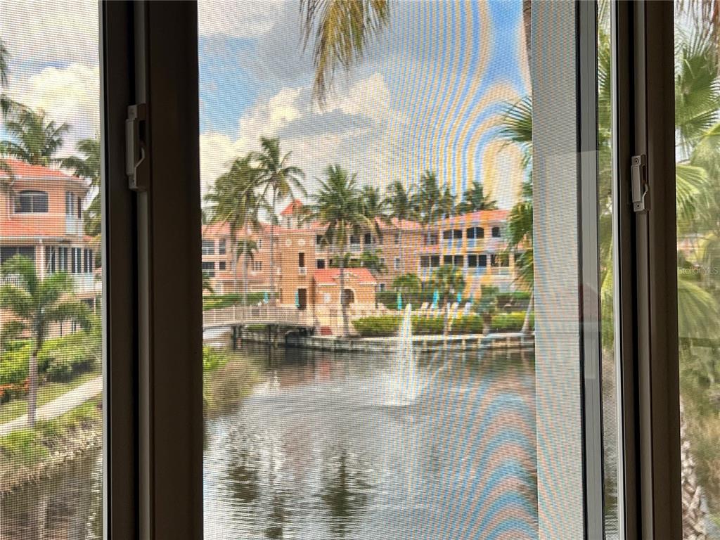 A view through a window screen shows a pond with a fountain and apartment buildings — 3304 SUNSET KEY CIRCLE UNIT D, PUNTA GORDA, FL