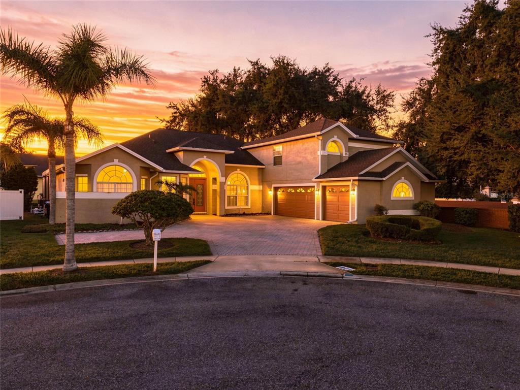 A two-story suburban house with a paved driveway and a palm tree at sunset — 10008 CANOPY TREE COURT, ORLANDO, FL