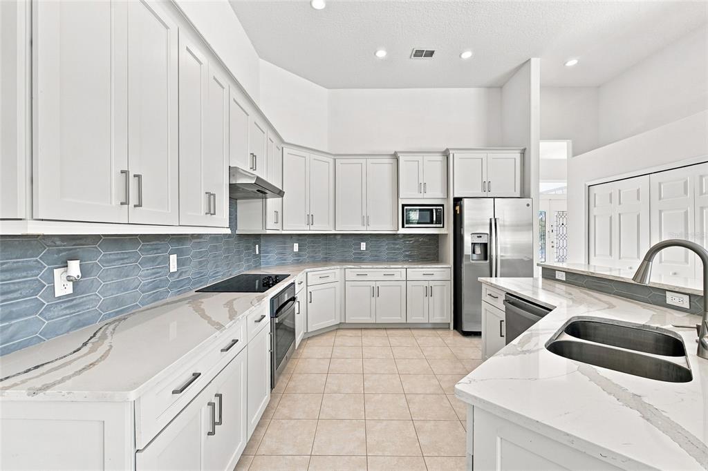 A kitchen features white cabinets, quartz countertops, a blue tiled backsplash, and stainless steel appliances — 10008 CANOPY TREE COURT, ORLANDO, FL