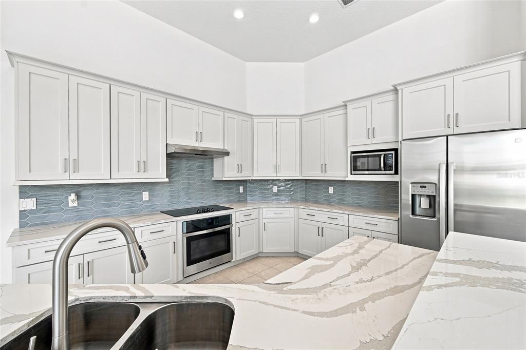 A kitchen with white cabinets, stainless steel appliances, blue tile backsplash, and quartz countertops — 10008 CANOPY TREE COURT, ORLANDO, FL