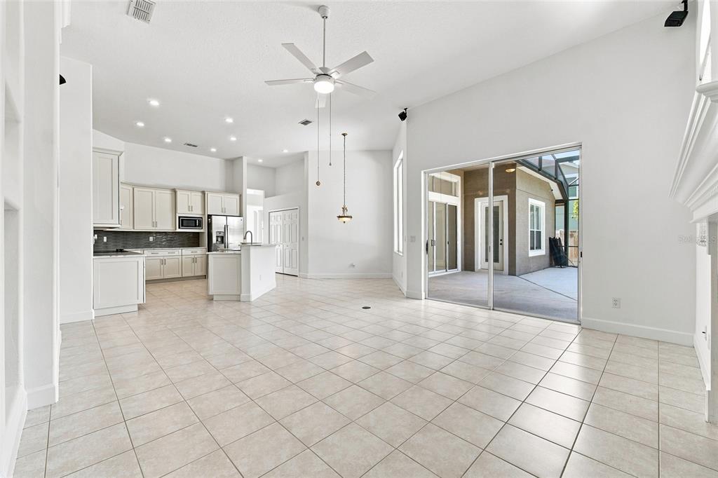 A bright, open-concept kitchen and living area with white cabinetry, tile flooring, and sliding doors — 10008 CANOPY TREE COURT, ORLANDO, FL