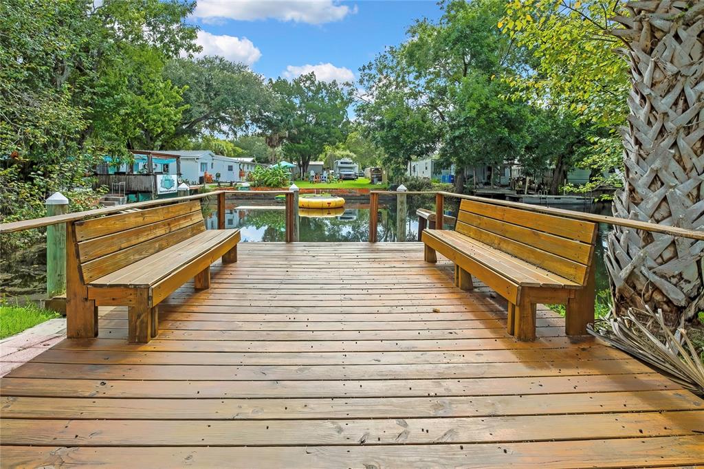A wooden deck features two built-in benches overlooking a canal with trees and mobile homes — 5610 RAMADA STREET, WEEKI WACHEE, FL