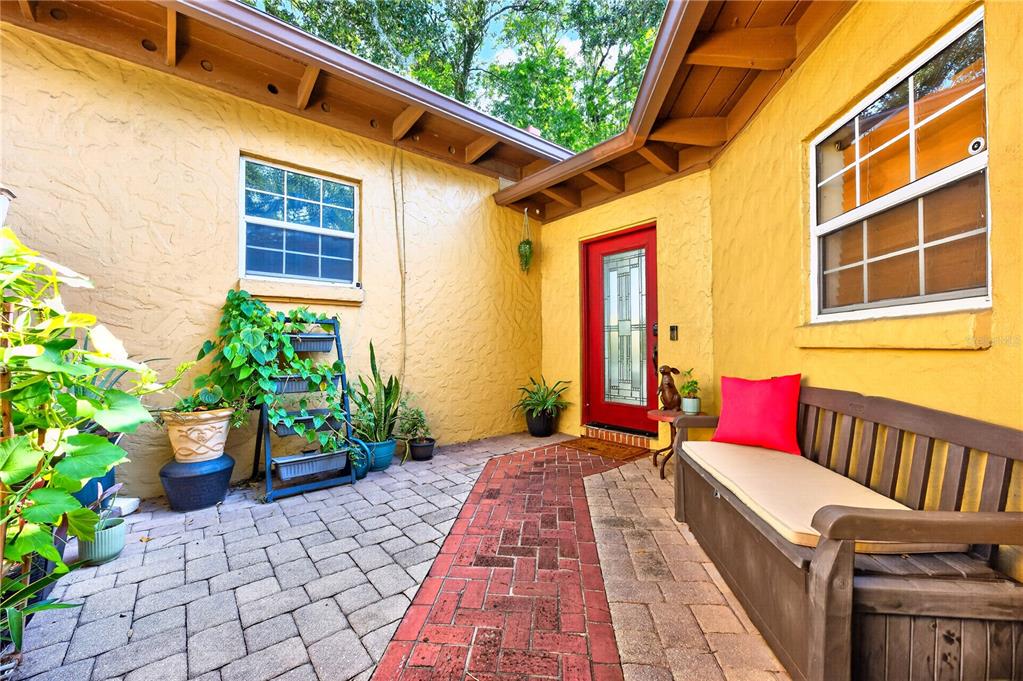 A brick-paved courtyard entrance features a red front door, a wooden bench, and potted plants — 1835 OAK LANE, ORLANDO, FL