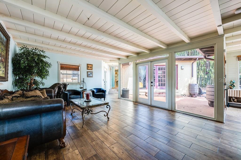 A living room with wood-look tile floors, a beamed ceiling, and glass doors to a patio — 1835 OAK LANE, ORLANDO, FL