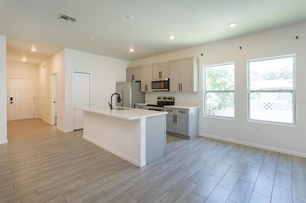 A modern kitchen features gray cabinets, white countertops, a central island, and light wood-look flooring — 1022 36TH, ORLANDO, FL