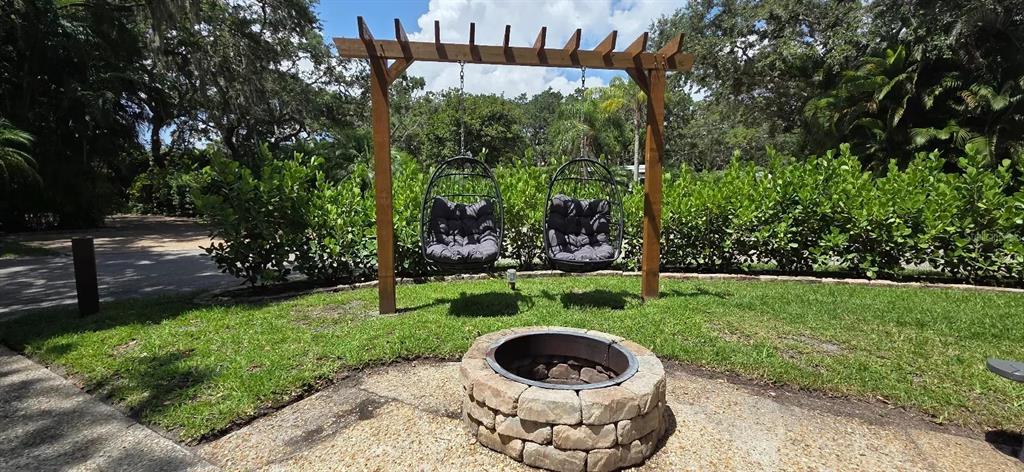 A stone fire pit sits in front of two hanging egg chairs suspended from a pergola — 374 BEAR TRAIL, RIVER RANCH, FL