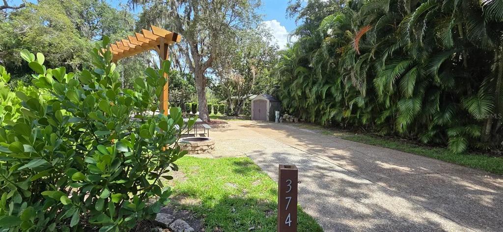A wooden pergola stands over a stone fire pit near a driveway and a shed — 374 BEAR TRAIL, RIVER RANCH, FL