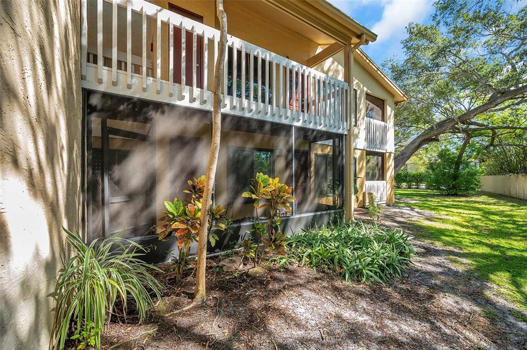 A ground-level screened-in patio sits beneath a second-story balcony on a tan stucco building — 1550 S BELCHER ROAD UNIT 117, CLEARWATER, FL