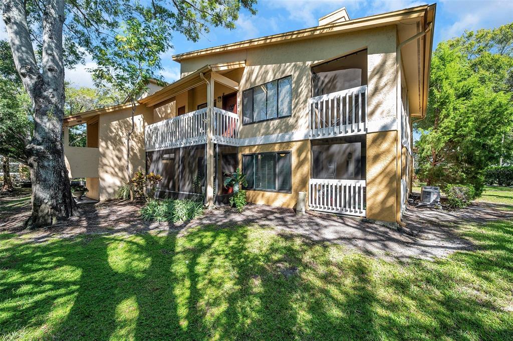 A two-story yellow stucco apartment building with screened-in balconies and a large tree nearby — 1550 S BELCHER ROAD UNIT 117, CLEARWATER, FL