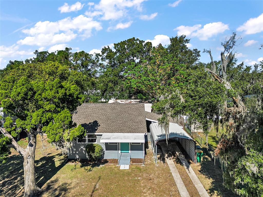 An aerial view of a single-story house with a metal carport and surrounding trees — 105 W STEVENS AVENUE, EUSTIS, FL