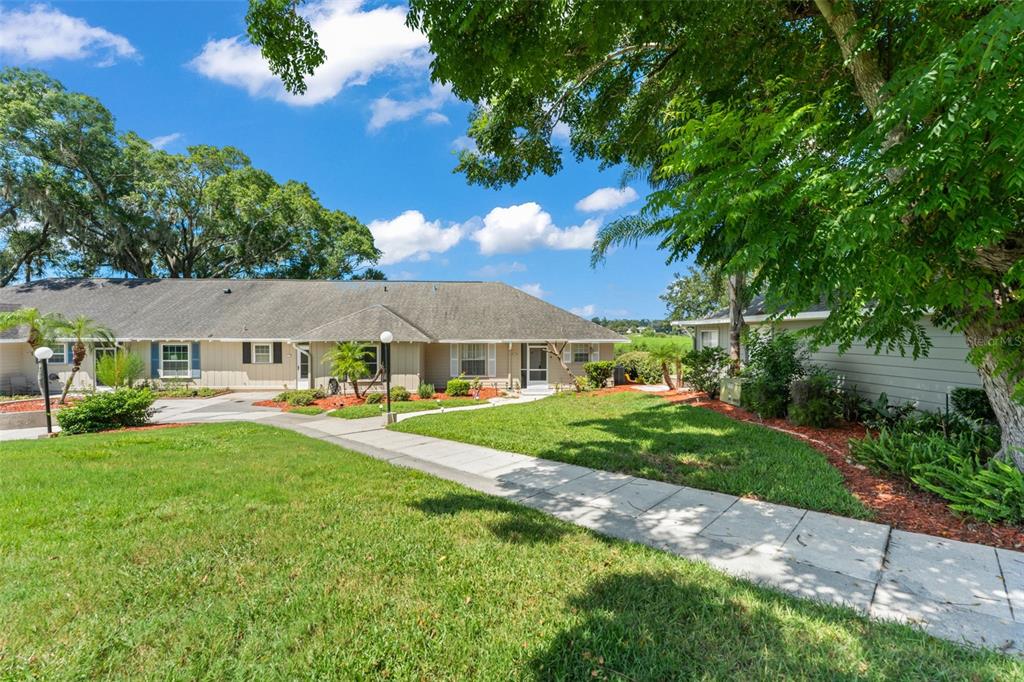 A single-story residential building with a gray roof and light siding sits behind a lawn — 1076 VILLA LANE UNIT 68, APOPKA, FL