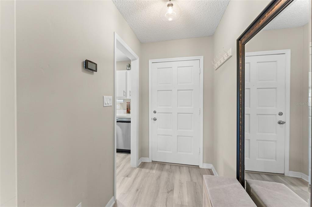 An entryway features light wood-look flooring, a white door, a wall mirror, and a ceiling light — 1076 VILLA LANE UNIT 68, APOPKA, FL