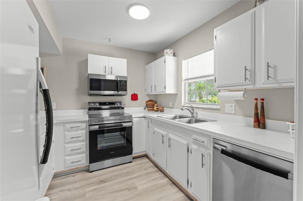 A kitchen features white cabinets, stainless steel appliances, light countertops, and wood-look flooring — 1076 VILLA LANE UNIT 68, APOPKA, FL