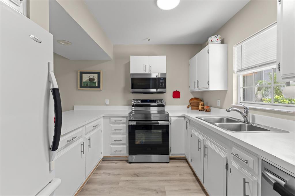 A kitchen with white cabinets, stainless steel appliances, and light-colored wood-look flooring — 1076 VILLA LANE UNIT 68, APOPKA, FL