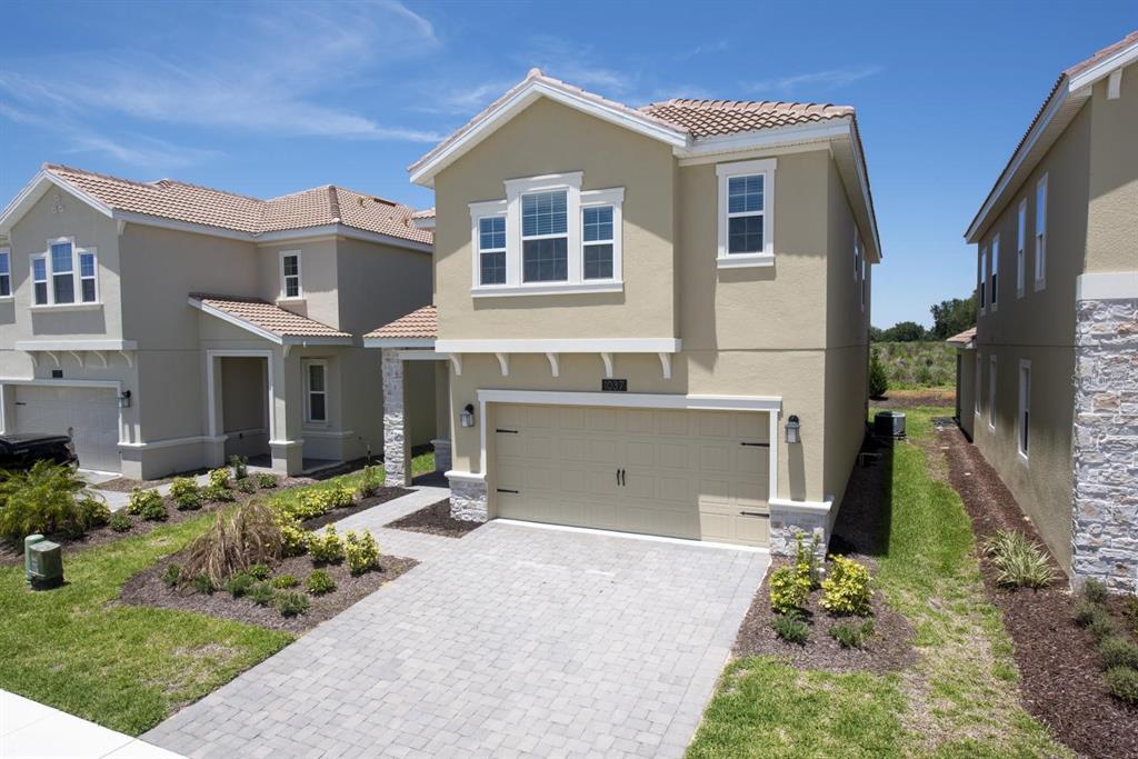A two-story suburban house with a tan stucco exterior, tile roof, and paved driveway — 1037 BLACKWOLF RUN ROAD, DAVENPORT, FL