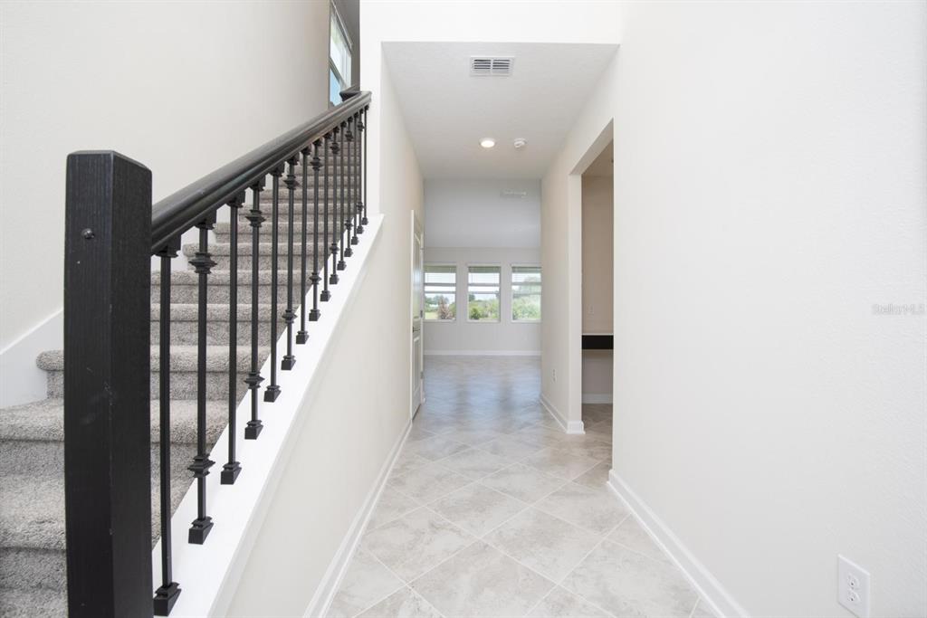 A hallway with tile flooring leads to a staircase with black railings and carpeted steps — 1037 BLACKWOLF RUN ROAD, DAVENPORT, FL