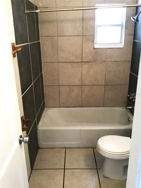 A bathroom features a white bathtub, a toilet, and walls with tan and dark tiles — 2226 27TH STREET S, ST PETERSBURG, FL