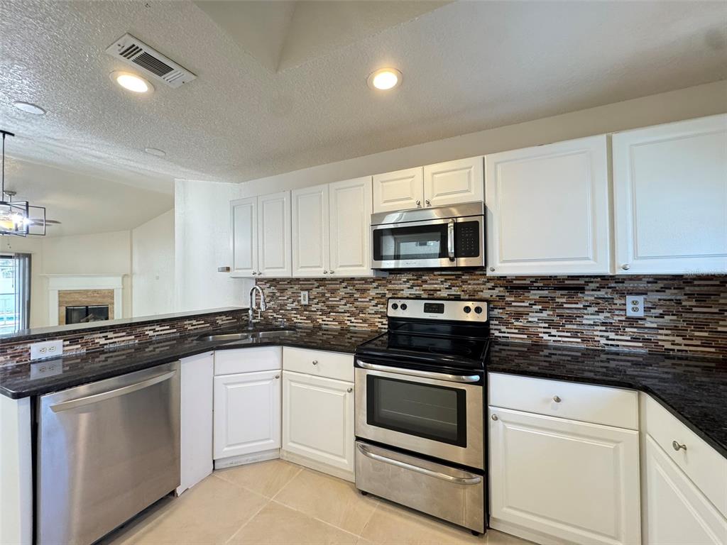 A kitchen features white cabinets, dark granite countertops, stainless steel appliances, and a tiled backsplash — 14 YORK COURT, KISSIMMEE, FL